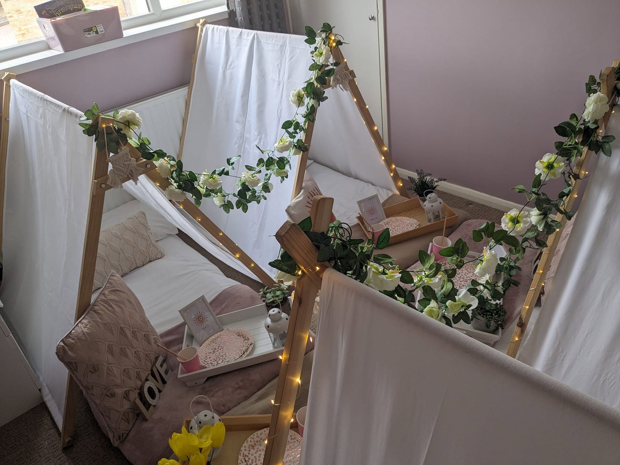 White sleepover teepees decorated with green foliage and warm lights