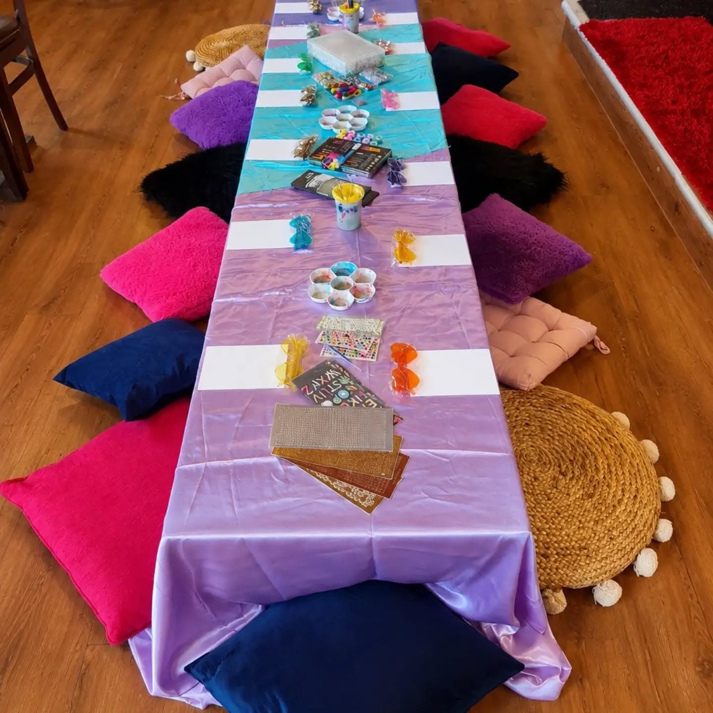 Long indoor craft table with colourful materials and bright floor cushions